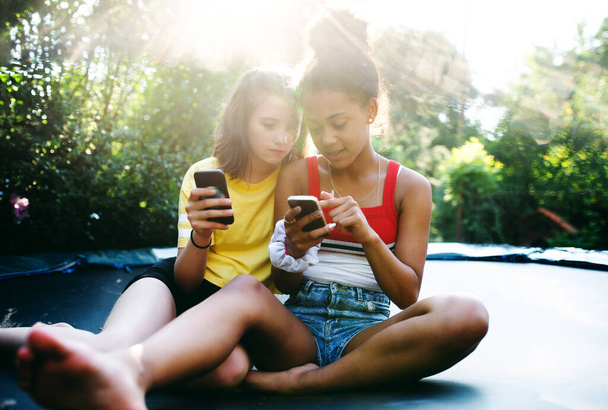 Front view of young teenager girls friends outdoors in garden, using smartphone. - Foto, afbeelding