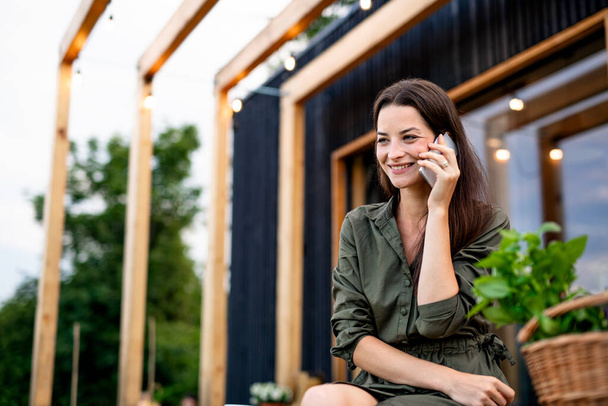 Young woman with smartphone outdoors, weekend away in container house in countryside. - Foto, Bild