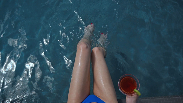 κορυφαία άποψη της υγρής γυναίκας με μαγιό που κάθεται κοντά στην πισίνα με κοκτέιλ  - Πλάνα, βίντεο