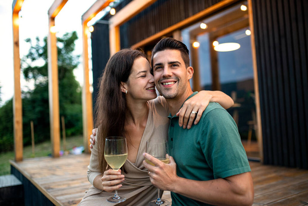 Young couple with wine outdoors, weekend away in container house in countryside. - Fotoğraf, Görsel