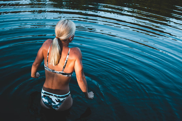 Ξανθιά κοπέλα μπαίνει στο νερό για να κολυμπήσει, κρυώνει.. - Φωτογραφία, εικόνα