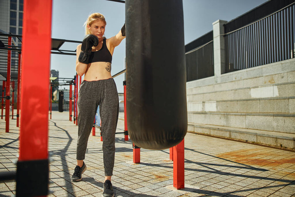 Extreme long shot of attractive sportive female is punching by left boxing glove during a kikcboxing training on the sports ground - Fotó, kép