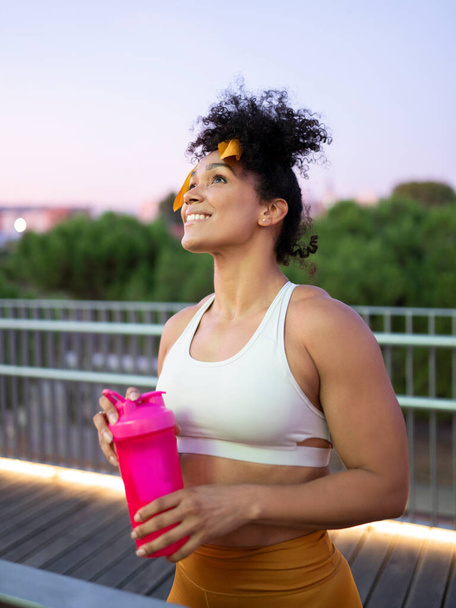 運動で失われた強さと栄養を取り戻すために公園で屋外で訓練した後、黒人女性はタンパク質を飲みます - 写真・画像