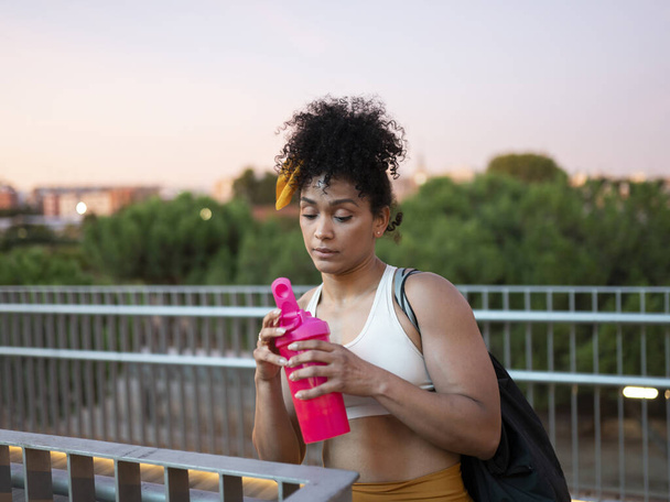 fekete nő iszik fehérje után szabadtéri edzés a parkban, hogy visszanyerje erejét - Fotó, kép