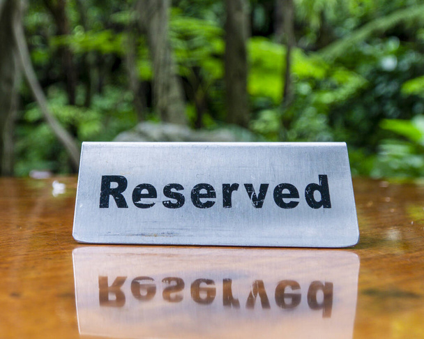 Зарезервированная табличка из нержавеющей стали на ламинированном деревянном столе ресторана с деревьями и лесом на заднем плане. - Фото, изображение