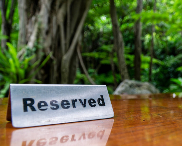Zarezerwowany znak wykonany z blachy ze stali nierdzewnej na laminowanym drewnianym stole restauracji z drzewami i lasem w tle. - Zdjęcie, obraz
