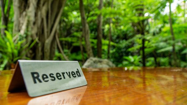 Segnale riservato in lamiera di acciaio inox su un tavolo di legno laminato di un ristorante con alberi e bosco sullo sfondo. - Foto, immagini