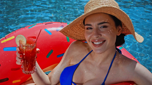 rack focus kobiety trzymającej koktajl i leżącej na pierścieniu pływackim w basenie  - Materiał filmowy, wideo
