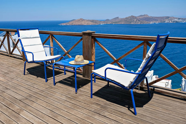 деревянная терраса виллы или отеля с двумя белыми стульями и столом и видом на море - Фото, изображение