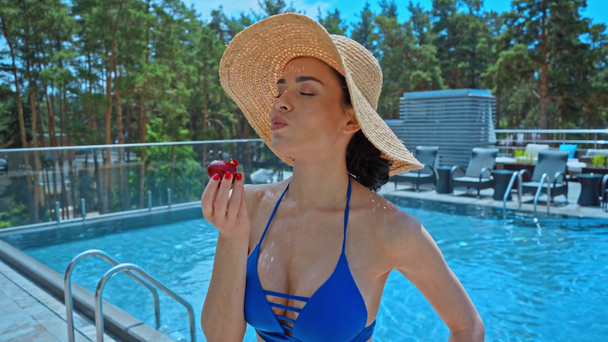 νεαρή γυναίκα με ψάθινο καπέλο τρώει δαμάσκηνο κοντά στην πισίνα  - Πλάνα, βίντεο