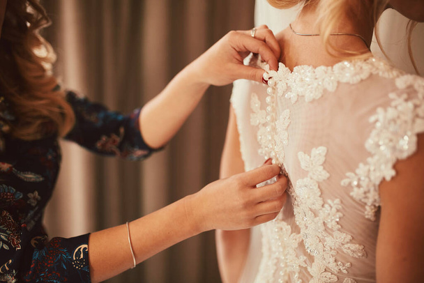 結婚式。新婦付添人は結婚式の日のために花嫁を準備する。花嫁介添人は儀式の前にドレスを固定するのに役立ちます。豪華なブライダルドレスを閉じます - 写真・画像