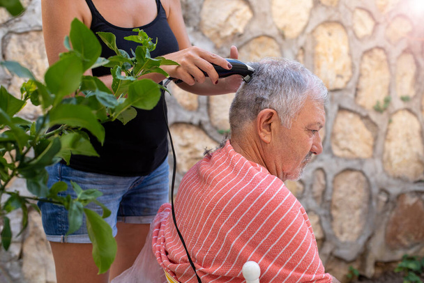 Concepto de corte de cabello en casa debido al virus corona. Una mujer está cortando el pelo de su padre. - Foto, imagen