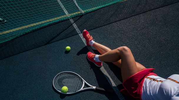 A faceless girl in a sports skirt sits on a tennis court and holds a rocket. Top view of female legs. - Fotoğraf, Görsel