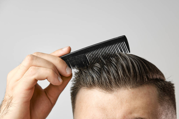 Gros plan jeune homme se brossant les cheveux avec un peigne en plastique. Coiffure après salon de coiffure. Soins capillaires. Concept de perte de cheveux - Photo, image