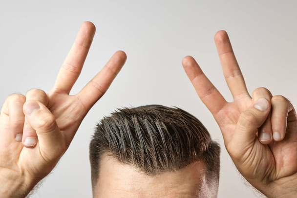 Homme avec une coupe de cheveux moderne et élégant après salon de coiffure montre signe de paix avec deux mains sous sa tête avec espace de copie. Soins de santé pour les cheveux. Hommes beauté.  - Photo, image