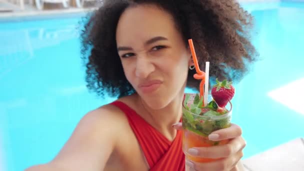 Mladá dívka teenager internet vlogger pózuje před kamerou s koktejlem v bazénu, ohne rty jako kachna, mrkne, oddává se pohyby, natáčení v první osobě. Live online stream from rest - Záběry, video