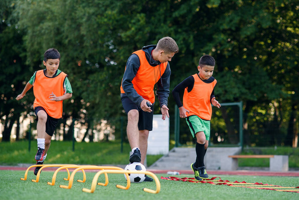Active teen footballers train together on artificial soccer field and follow the instructions of a professional coach. - Foto, Imagem