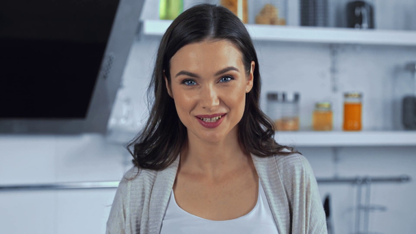 Νεαρή γυναίκα κοιτάζει κάμερα στην κουζίνα  - Πλάνα, βίντεο