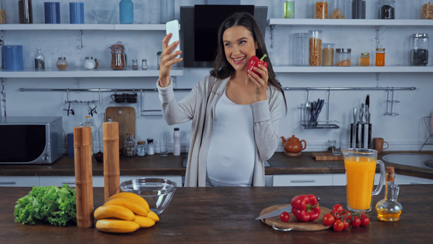 Donna incinta che scatta foto con smartphone vicino alle verdure in cucina  - Filmati, video