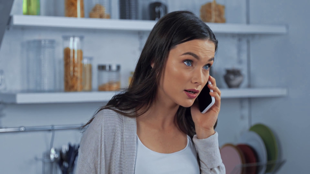 Vihainen brunette nainen puhuu älypuhelimella keittiössä  - Materiaali, video