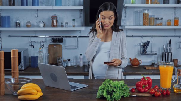 Kobieta w ciąży rozmawia na smartfonie podczas zakupów online w kuchni  - Materiał filmowy, wideo