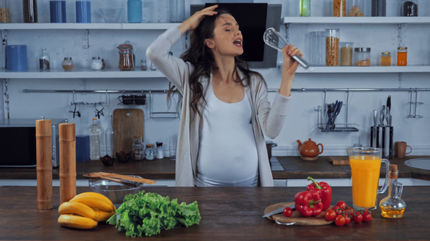 Έγκυος γυναίκα με χτυπημένο σύρμα χορεύει και τραγουδάει κοντά στο φαγητό στην κουζίνα  - Πλάνα, βίντεο