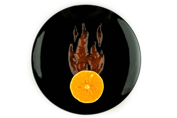 superscharfe getrocknete Orangenscheibe, in Flammen gehüllt, mit scharfer Chilisoße auf schwarzem Teller, isoliert auf weißem Teller, blendfrei - Foto, Bild