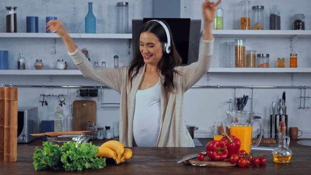 Вагітна жінка в навушниках танцює і співає біля овочів на кухні
  - Кадри, відео