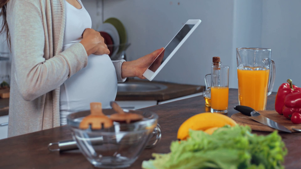 Καλλιεργημένη άποψη της εγκύου γυναίκα χρησιμοποιώντας ψηφιακή ταμπλέτα, ενώ το μαγείρεμα στην κουζίνα  - Πλάνα, βίντεο