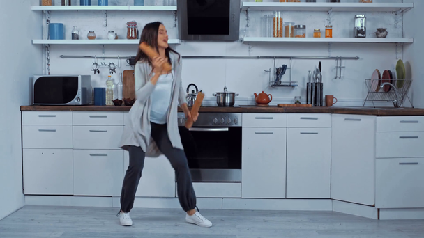 Mujer embarazada joven bailando con pimienta y molinos de sal en la cocina - Imágenes, Vídeo