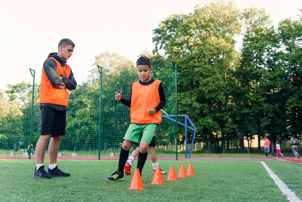 Motivated sporty 13-s boys in orange vests running among the plastic cones during soccer training at the stadium. - Zdjęcie, obraz