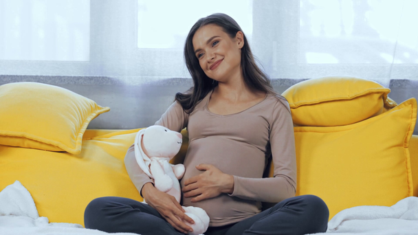 Mulher grávida tocando barriga e segurando brinquedo macio em casa - Filmagem, Vídeo