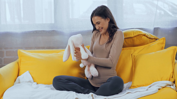 Donna incinta che tiene il giocattolo morbido sul divano  - Filmati, video