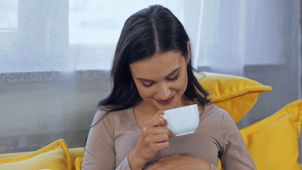 Беременная женщина пьет чай на диване   - Кадры, видео