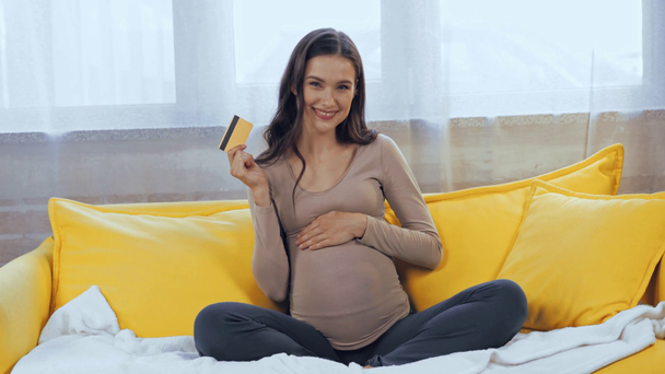 Mulher grávida segurando cartão de crédito e tocando barriga no sofá - Filmagem, Vídeo