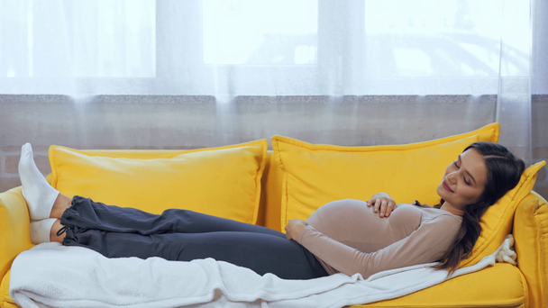 Έγκυος γυναίκα αγγίζει την κοιλιά ενώ κοιμάται στον καναπέ  - Πλάνα, βίντεο