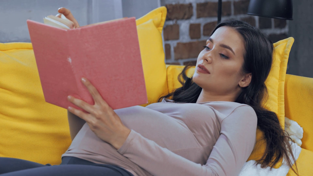 Kobieta w ciąży czyta książkę na kanapie  - Materiał filmowy, wideo