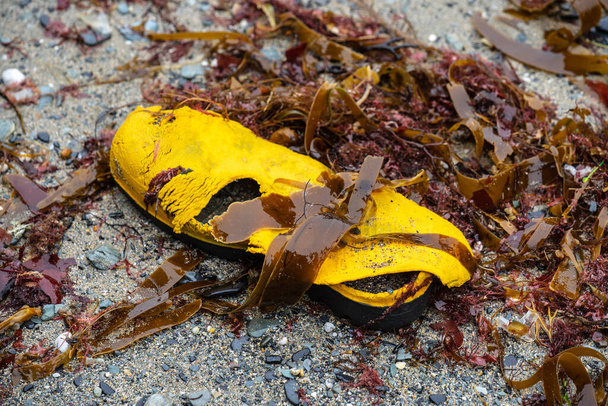 Мусор, выброшенный из моря волнами на берег. Старая желтая обувь - Фото, изображение