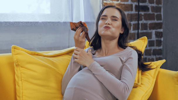 Mujer embarazada comiendo magdalena en el sofá  - Metraje, vídeo