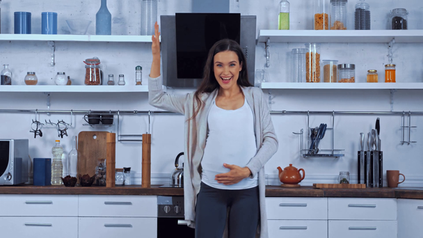 Raskaana oleva nainen elehtii ja koskettaa vatsa keittiössä  - Materiaali, video