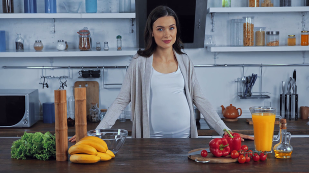 Kobieta w ciąży stojąca w pobliżu jedzenia i soku pomarańczowego w kuchni  - Materiał filmowy, wideo