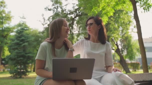 Jonge vrouw die haar oude gepensioneerde moeder helpt op een laptop in een park. Concept van Leeftijd Inclusiviteit. Slow motion shot - Video