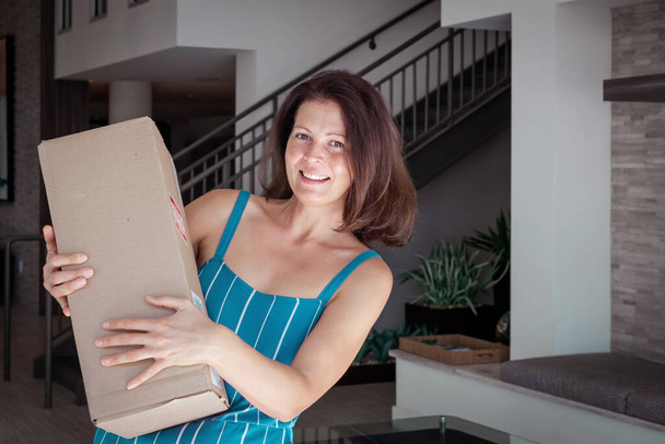 Mulher sorridente carregando uma caixa de encomendas em casa, entrega de mercadorias e conceito de pessoas. - Foto, Imagem