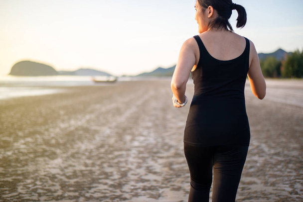 Fit asian woman running on the beach during sunset time - Photo, Image