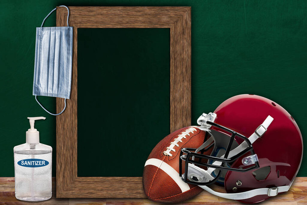 COVID-19木製テーブルのコピースペースとアメリカンフットボールとヘルメットと額装された黒板を示す教室の設定で新しい通常のスポーツコンセプト. - 写真・画像