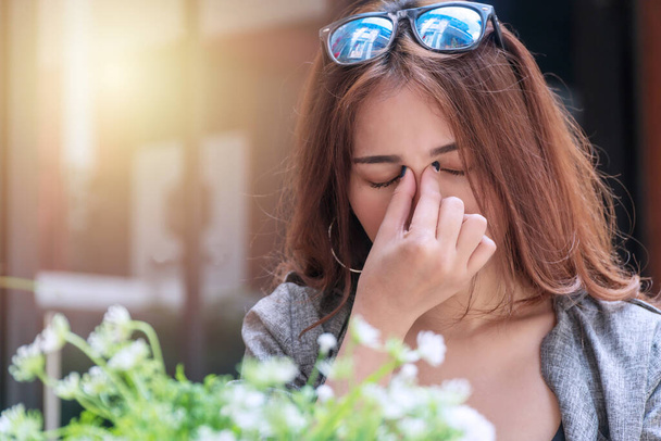 Tired young businesswoman massaging nose bridge feeling eye strain or headache trying to relieve pain. Overworked young woman have migraine feeling straining her eyes while sitting in garden. - Foto, Imagem