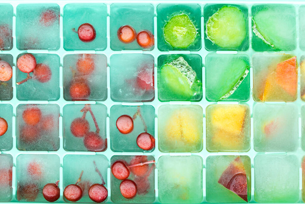 Silikon kalıpta sebze ve böğürtlen dolu buz küpleri. Buzların içinde dondurulmuş yenilebilir meyve.. - Fotoğraf, Görsel