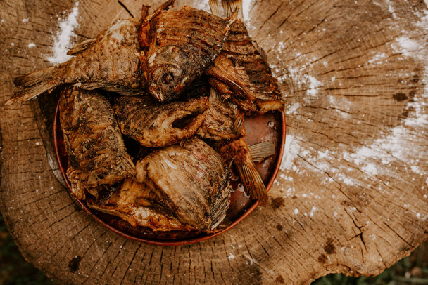 sült hal kereszt ponty fekszik egy tányéron egy régi repedt fa csonk - Fotó, kép