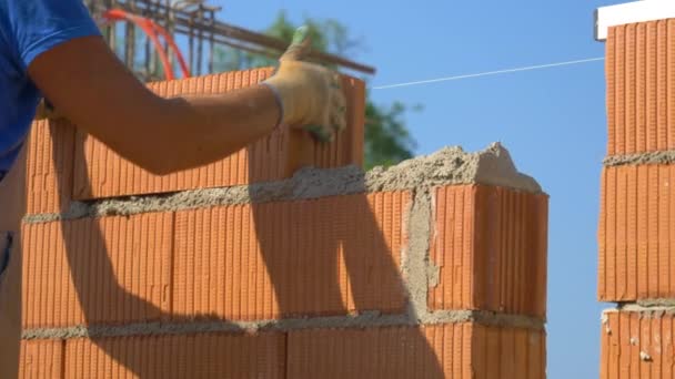 CERRAR: Albañil coloca un ladrillo en la parte superior de hormigón húmedo mientras se construye una pared - Metraje, vídeo