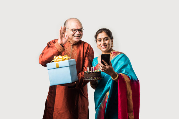 Indian cheerful old couple celebrating birthday with chocolate cake while wearing ethnic traditional cloths - Valokuva, kuva